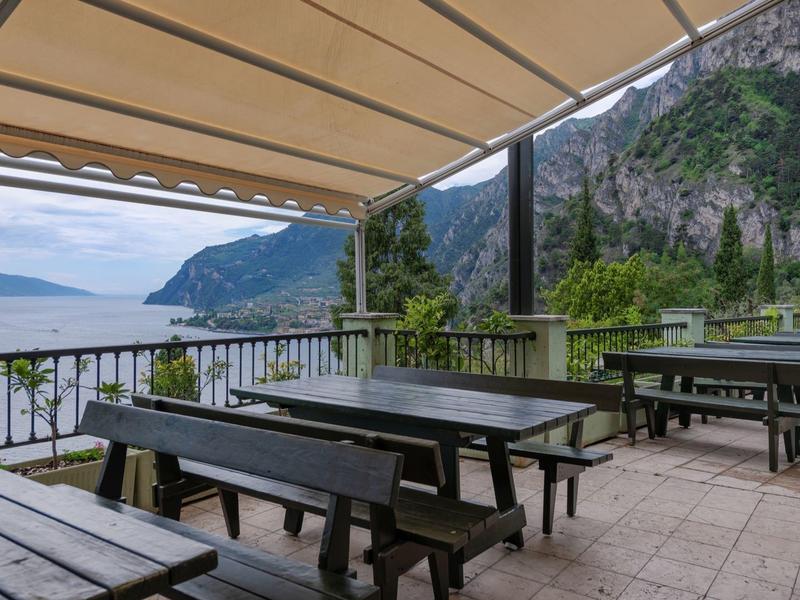 Pusta zewnętrzna taras z drewnianymi ławkami i stołami z widokiem na morze i góry.