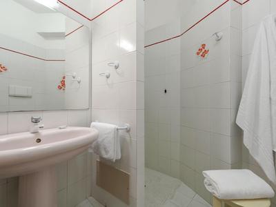 Kompaktní koupelna s bílými dlaždicemi, umyvadlem, sprchovým koutem a ručníky.