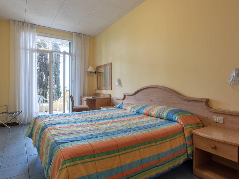 Hotelový pokoj se dvěma jednolůžky, barevnými přikrývkami a přístupem na balkon s výhledem ven.