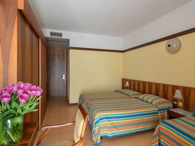 Chambre d'hôtel avec deux lits, des couvre-lits rayés et un bouquet de fleurs sur la table.