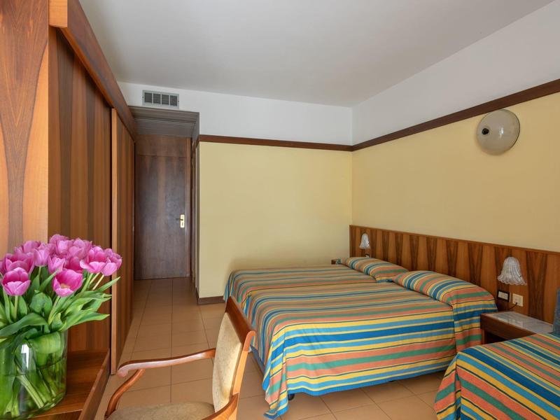 Chambre d'hôtel avec deux lits, des couvre-lits rayés et un bouquet de fleurs sur la table.