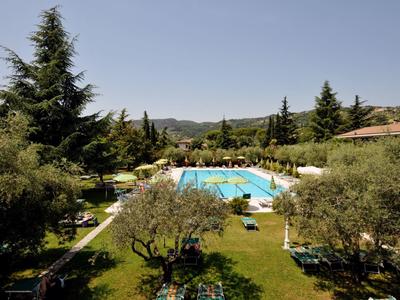 Uitzicht op een buitenzwembad met ligstoelen en bomen in een tuin bij heldere lucht.