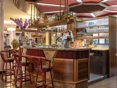 Gemütliche Bar mit Holztheke, roten Barhockern, Gläsern und Dekor in warmem Licht.