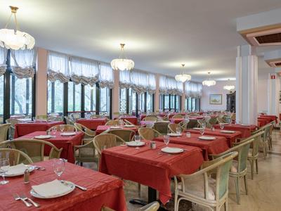 Großer Speisesaal mit roten Tischdecken und weißen Stühlen, große Fenster an der Seite.