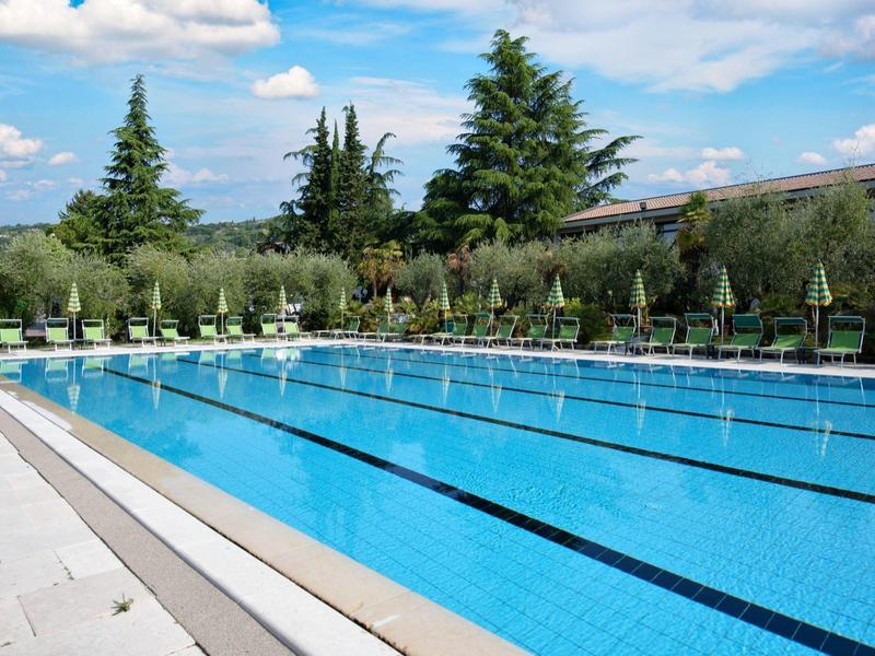 Een buitenzwembad met zwembanen en ligstoelen bij een hotel onder zonnige hemel.