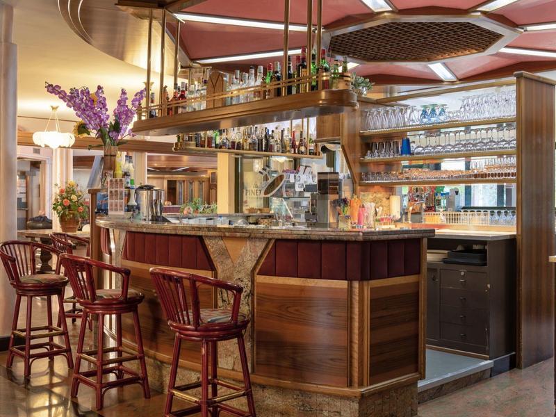 Elegante hotelbar met houten bar, barkrukken en planken vol glazen en flessen.