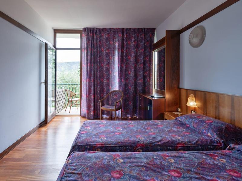 Hotelkamer met twee eenpersoonsbedden, houten vloer en balkon met uitzicht naar buiten.