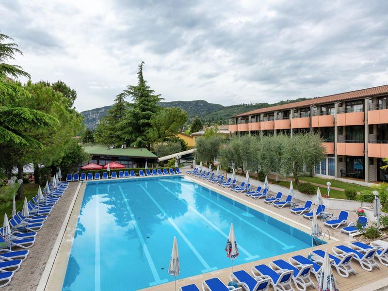 Grande piscine extérieure avec chaises longues bleues à côté d'un hôtel à plusieurs étages sous un ciel nuageux.