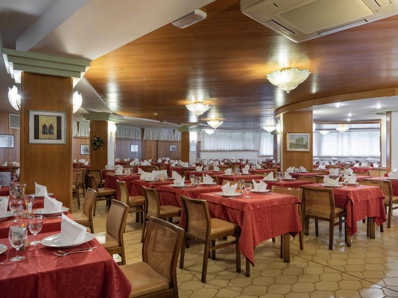 Grande salle de restaurant avec des tables recouvertes de rouge et des chaises en bois dans un cadre hôtelier.