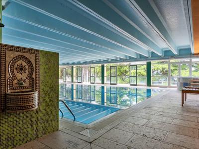 Interno di una piscina coperta con fontana d'acqua in mosaico e grandi finestre.
