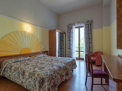 Camera d'hotel con letto matrimoniale, scrivania, sedia e balcone con vista esterna.