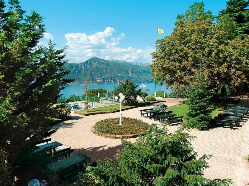 Giardino dell'hotel con tavoli e sedie, alberi e vista sulle montagne sullo sfondo