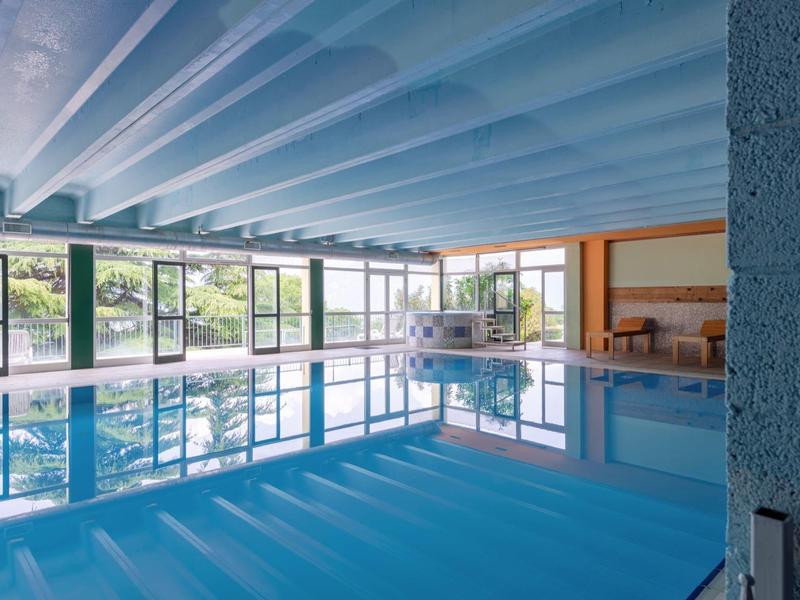 Spazio interno di un hotel con grande piscina e luce naturale attraverso grandi finestre.