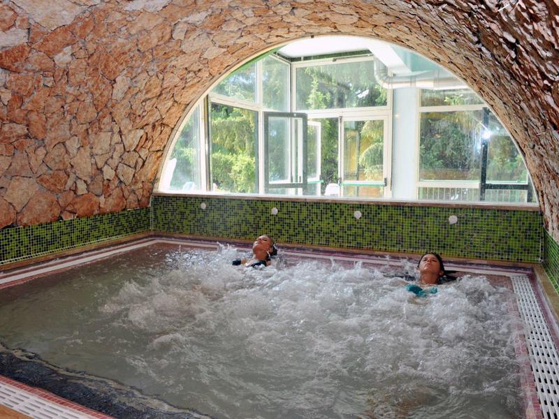 Vasca idromassaggio in una stanza rivestita di pietra con grande finestra e due persone dentro
