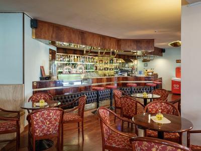 Accogliente bar dell'hotel con legno scuro, sedie in pelle e scaffalatura ben fornita sullo sfondo.