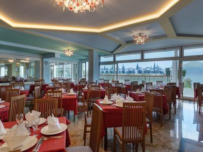 Geräumiges Restaurant mit Holzstühlen, roten Tischdecken und großen Fenstern mit Hafenblick.
