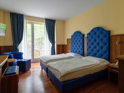 Camera d'hotel luminosa con due letti con testiere blu, una poltrona e un balcone.