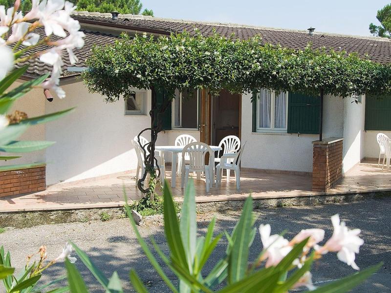 Ein Haus mit weißer Fassade, grünen Fensterläden und einer Terrasse mit weißen Plastikstühlen.