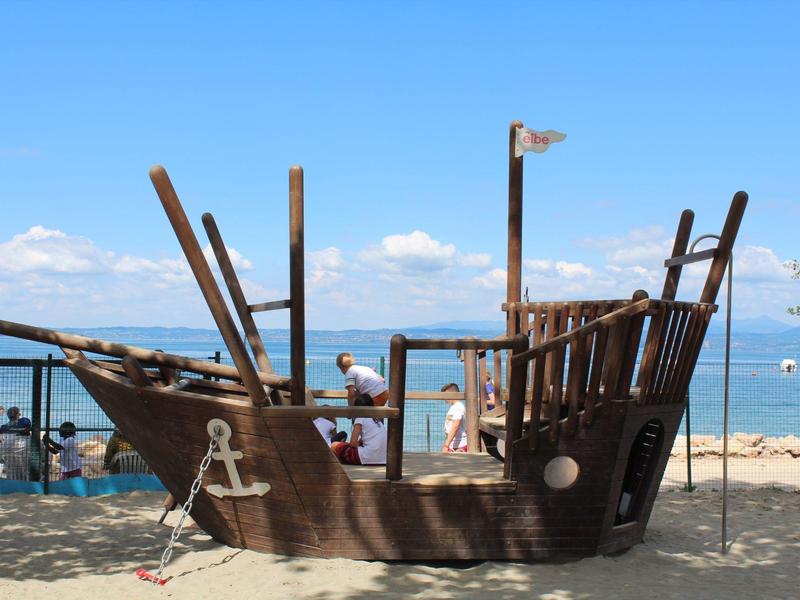 Holzspielplatz in Form eines Piratenschiffs am Strand mit Blick auf das Meer und blauen Himmel.