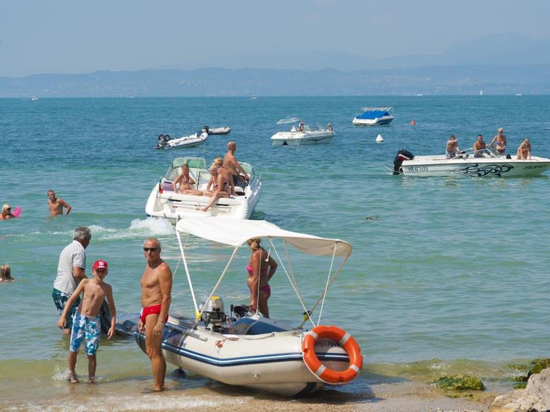 Strand mit Menschen im Wasser, kleinen Booten und einem Boot am Ufer mit Rettungsring.