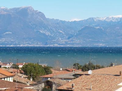 Dachlandschaft mit roten Ziegeln, dahinter ein großer See und Berge unter klarem Himmel.