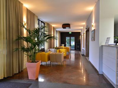 Heller Hotelflur mit Polstermöbeln in Gelb und grau, Pflanzen und modernem Empfangstresen.