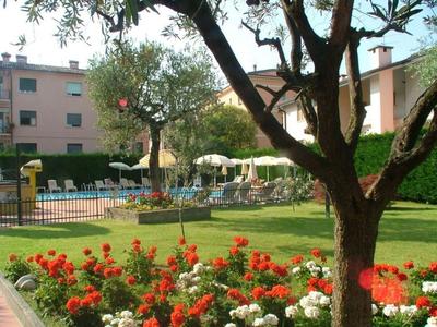 Grüner Garten mit blühenden Blumen, Bäumen und einem Swimmingpool vor Hotelgebäuden.