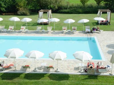 Una piscina rettangolare all'aperto con ombrelloni bianchi e sdraio su pavimentazione e prato.