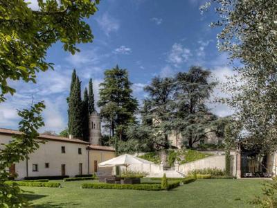 Giardino verde con prato curato e alberi davanti a un edificio chiaro sotto un cielo azzurro.