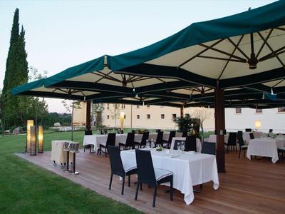 Area esterna dell'hotel con tavoli e sedie coperti sotto grandi ombrelloni su terrazza in legno.