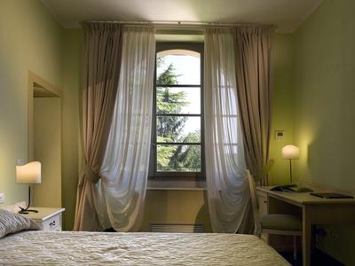 Camera d'hotel luminosa con letto, scrivania, lampada e grande finestra con tende.