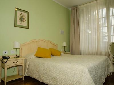 Camera d'hotel luminosa con letto matrimoniale, cuscini gialli, parete verde, comodino e finestra con tende.