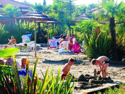 Kinderen spelen op het zandstrand van een tropisch hotel met ligstoelen en parasols.