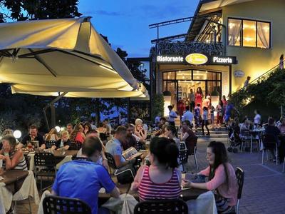 Avondterras met veel gasten buiten een hotel bij schemering.