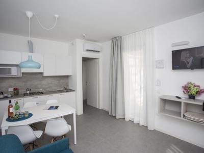 Modern eingerichtetes Hotelzimmer mit Küchenzeile, Esstisch und TV an der Wand.