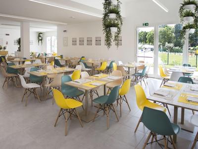 Hell und modern eingerichteter Speiseraum mit bunten Stühlen und großen Fenstern.