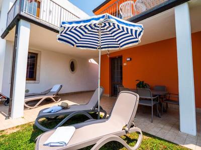 Terrasse mit Liegestühlen, blau-weiß gestreiftem Sonnenschirm und orangener Wand im Hintergrund.