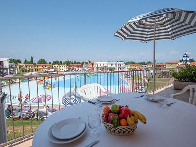Ausblick auf einen Pool und Garten in einer Hotelanlage, im Vordergrund ein Tisch mit Obstkorb und Sonnenschirm.