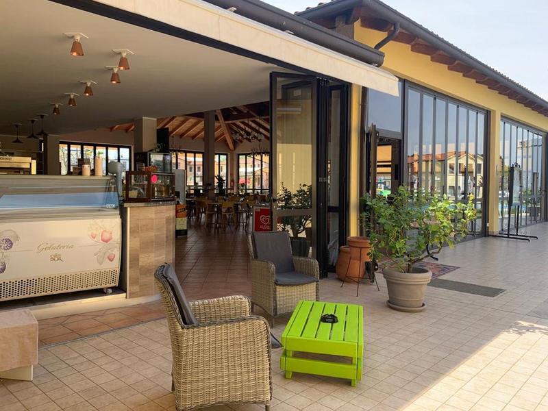 Area esterna moderna di un ristorante con posti a sedere e grandi finestre di vetro.