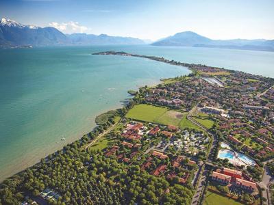 Letecký pohled na město u jezera s horami v pozadí a zalesněným břehem.