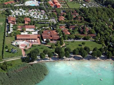 Luftaufnahme eines Hotels mit Pool, grünen Gärten und eigenem Zugang zu einem türkisfarbenen See.