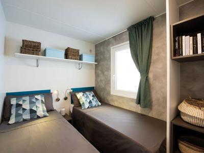 Modern eingerichtetes Hotelzimmer mit zwei Einzelbetten, grünem Vorhang und Regalen.