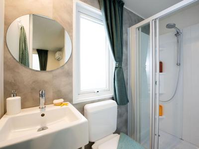 Modernes Hotelbadezimmer mit weißem Waschbecken, Spiegel und Duschkabine neben Fenster und Vorhang.