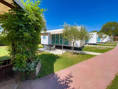 Moderner Ferienbungalow mit Terrasse auf gepflegtem Rasen und blauem Himmel.