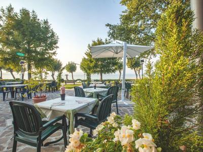 Außenterrasse mit gedeckten Tischen, Stühlen und Sonnenschirmen in einem grünen Garten.