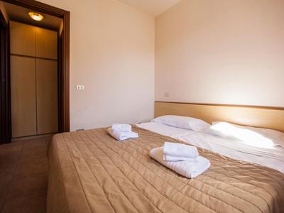 Jednoduchý hotelový pokoj se dvěma jednolůžky, hnědou přikrývkou a bílými ručníky.