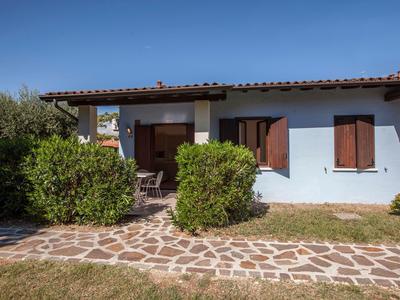 Rodinný dům s modrými zdmi, červenou střechou a obklopený keři pod jasnou oblohou