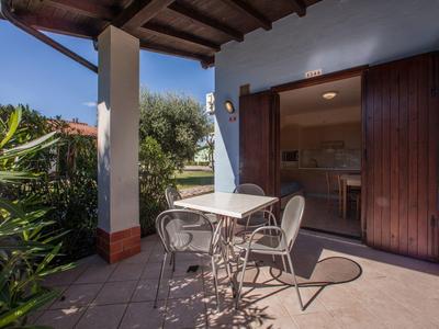 Terasa se stolkem a židlemi před otevřenými dřevěnými dveřmi domu za slunečného dne