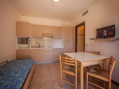 Malý byt s kuchyňským koutem, jídelním stolem, židlemi a pohovkou s modrou matrací.