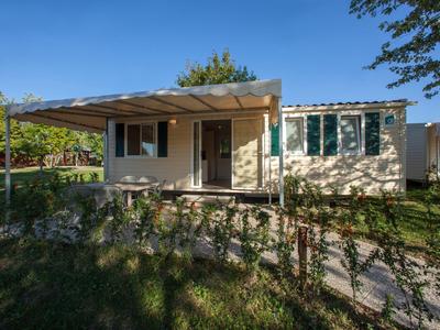 Bungalov s verandou a zahradou na slunném místě pod modrou oblohou.